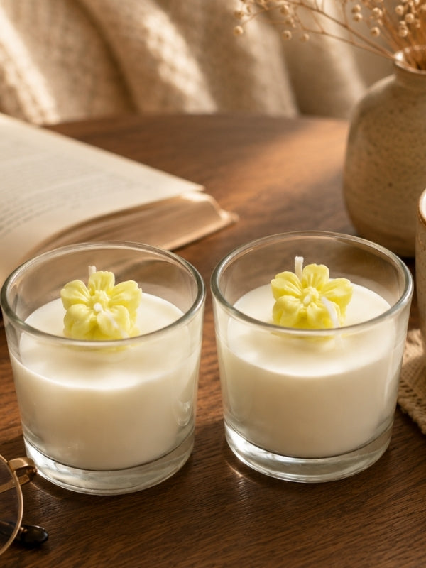 Set of two handcrafted scented soy wax candles in clear glass jars, each measuring approximately 2.25 inches in diameter and 2.25 inches in height, decorated with yellow wax flowers on the surface.