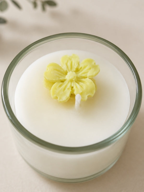 Close-up of the handcrafted soy wax candle showing the yellow wax flower decoration, smooth wax finish, and clear glass container.