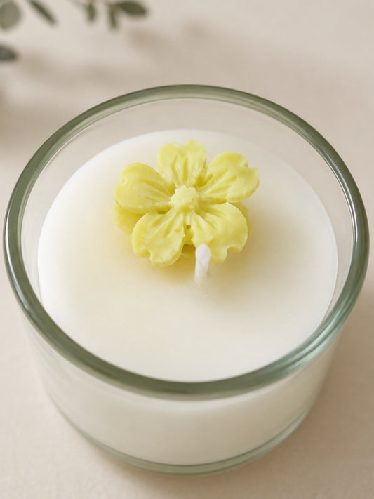 Close-up of the handcrafted soy wax candle showing the yellow wax flower decoration, smooth wax finish, and clear glass container.