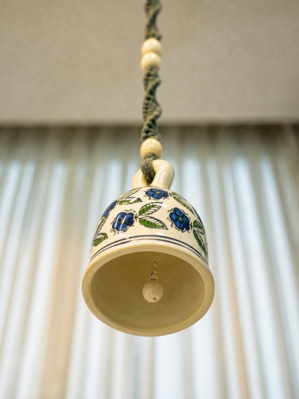Angled view of the ceramic macramé bell hanging showing the large ceramic bell, handcrafted knot work, and hanging structure.
