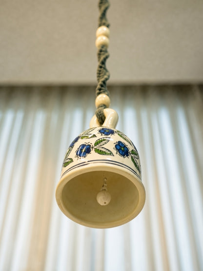 Angled view of the ceramic macramé bell hanging showing the large ceramic bell, handcrafted knot work, and hanging structure.

