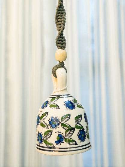 Close-up of the handcrafted ceramic bell highlighting the painted finish, wooden beads, and intricate macramé knots.
